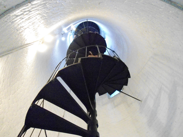 A black metal spiral staircase rises up in the middle of a white tower