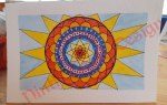 rectangular paper with a mandala shaped to fit the space in yellows and reds, with blues and purple, blue background