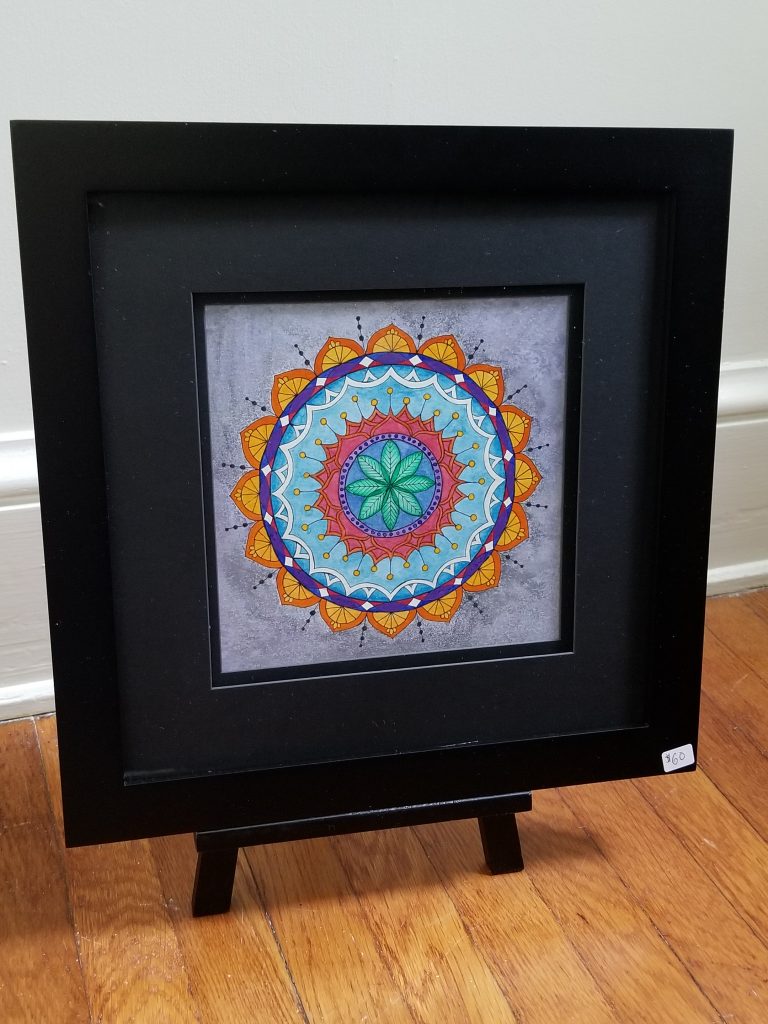 photograph of a framed mandala on a wooden floor near a white wall